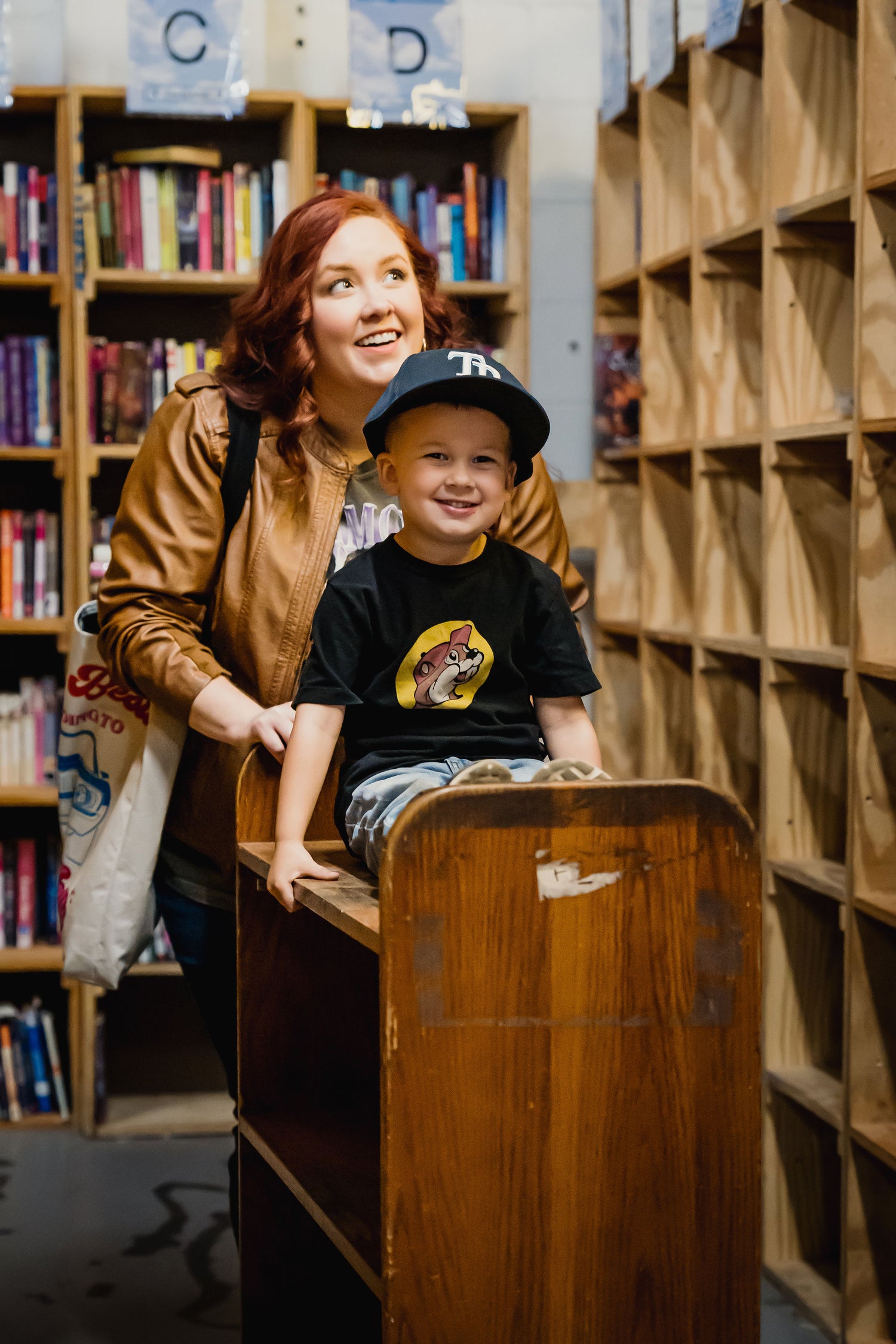 woman pushing smiling little boy through aisles of books