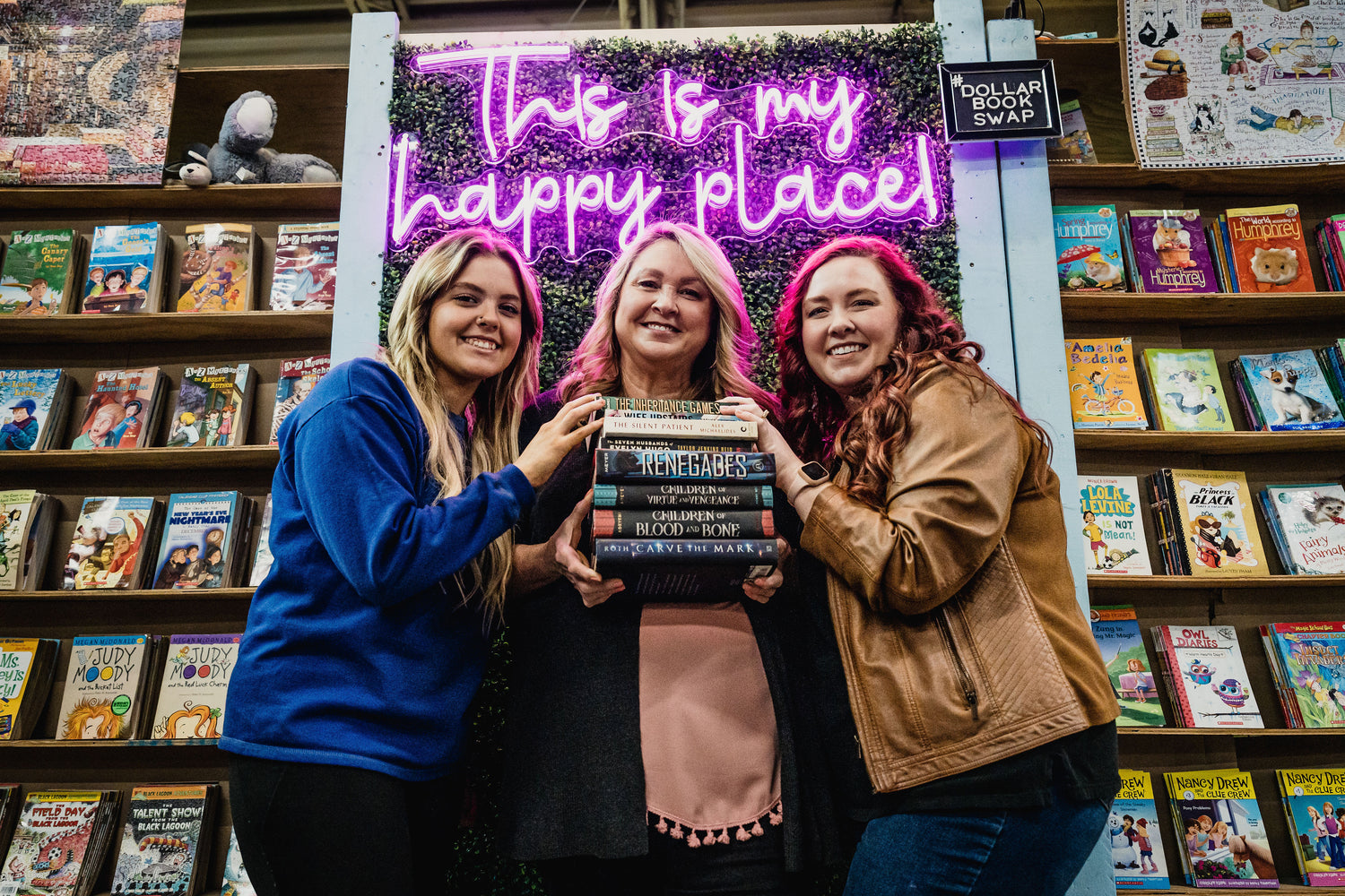 3 women holding a stack of books and smiling