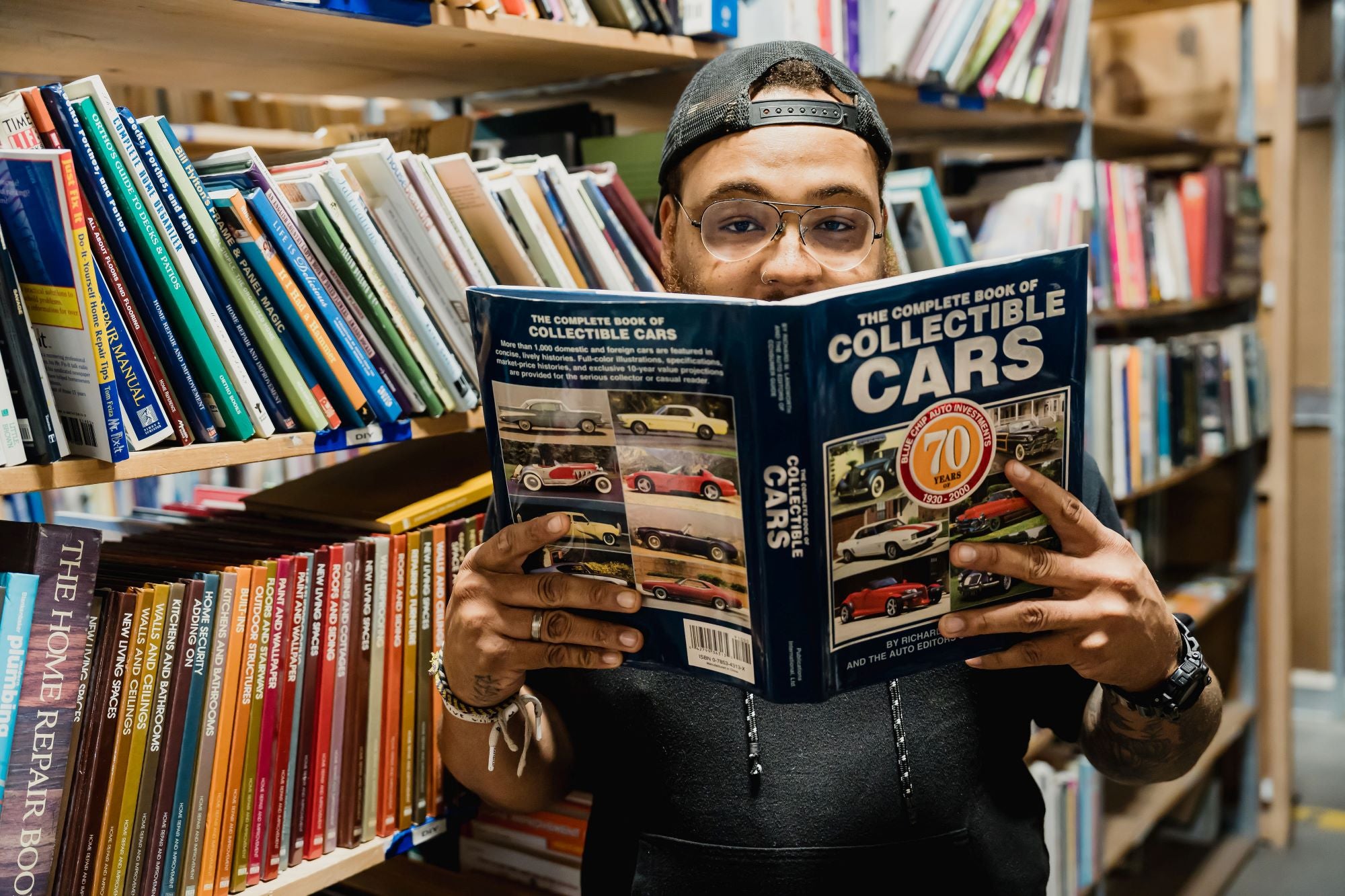 person holding up book about collectible cars and looking at camera